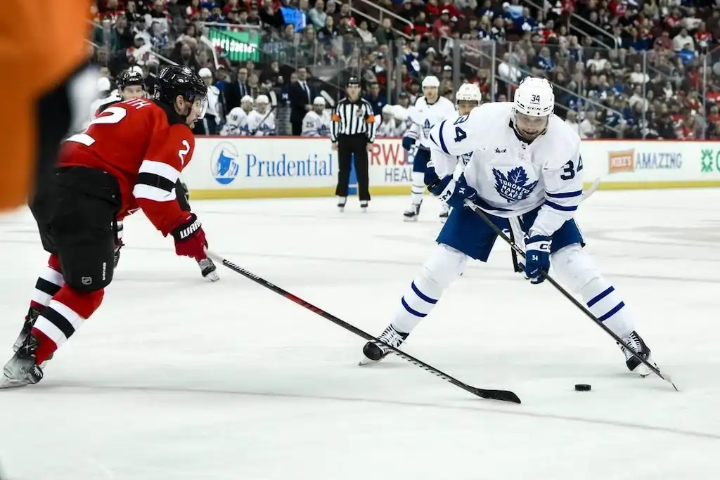 A Toronto Maple Leafs player controls the puck while being defended by a New Jersey Devils player.