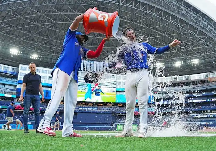 A Blue Jays Baseball player pours a cooler of water over a teammate in celebration on the field.