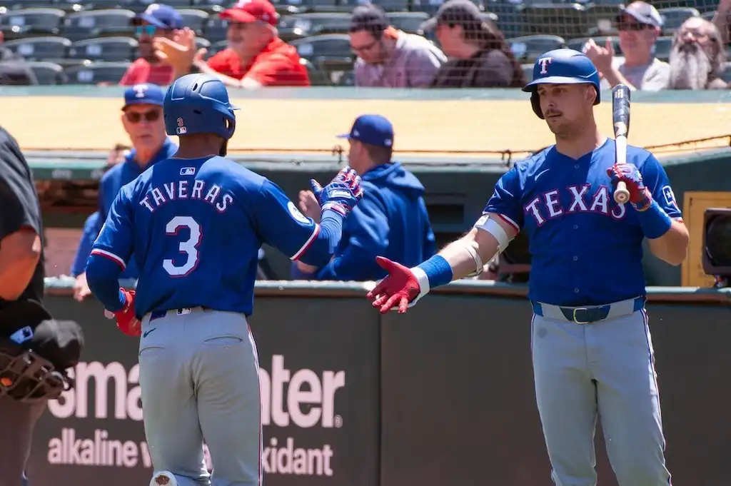 3 Texas Rangers baseball players exchange a fist bump near the dugout.