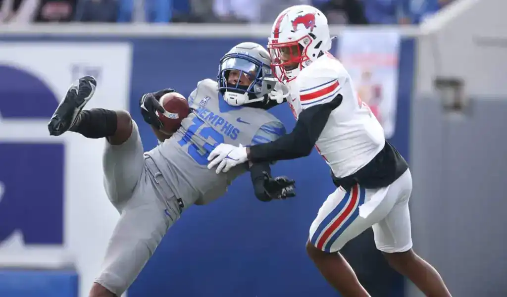 Jugadores de fútbol americano universitario en acción durante un partido de la Conferencia AAC 2024, con enfoque en una jugada de recepción.