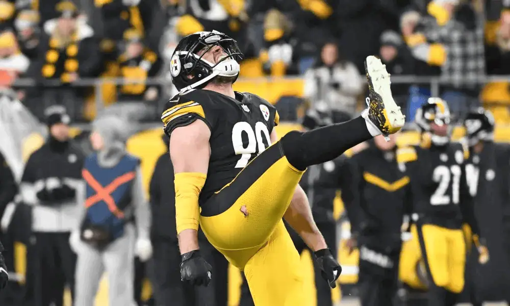 A football player in a black and yellow jersey celebrates energetically, raising one leg and expressing excitement in a packed stadium.
