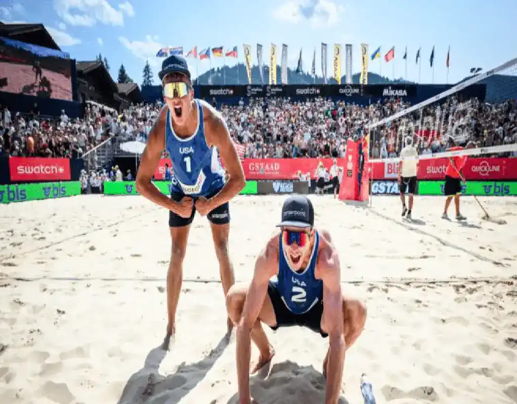 USA men's beach volleyball players celebrate a point during an international tournament in front of a large crowd.