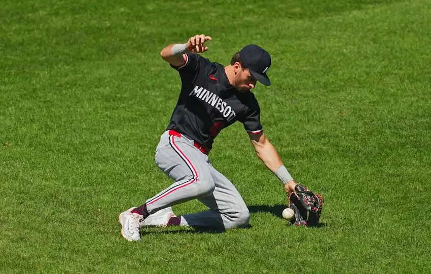 Minnesota baseball player attempts to field a ground ball while kneeling on the outfield grass.