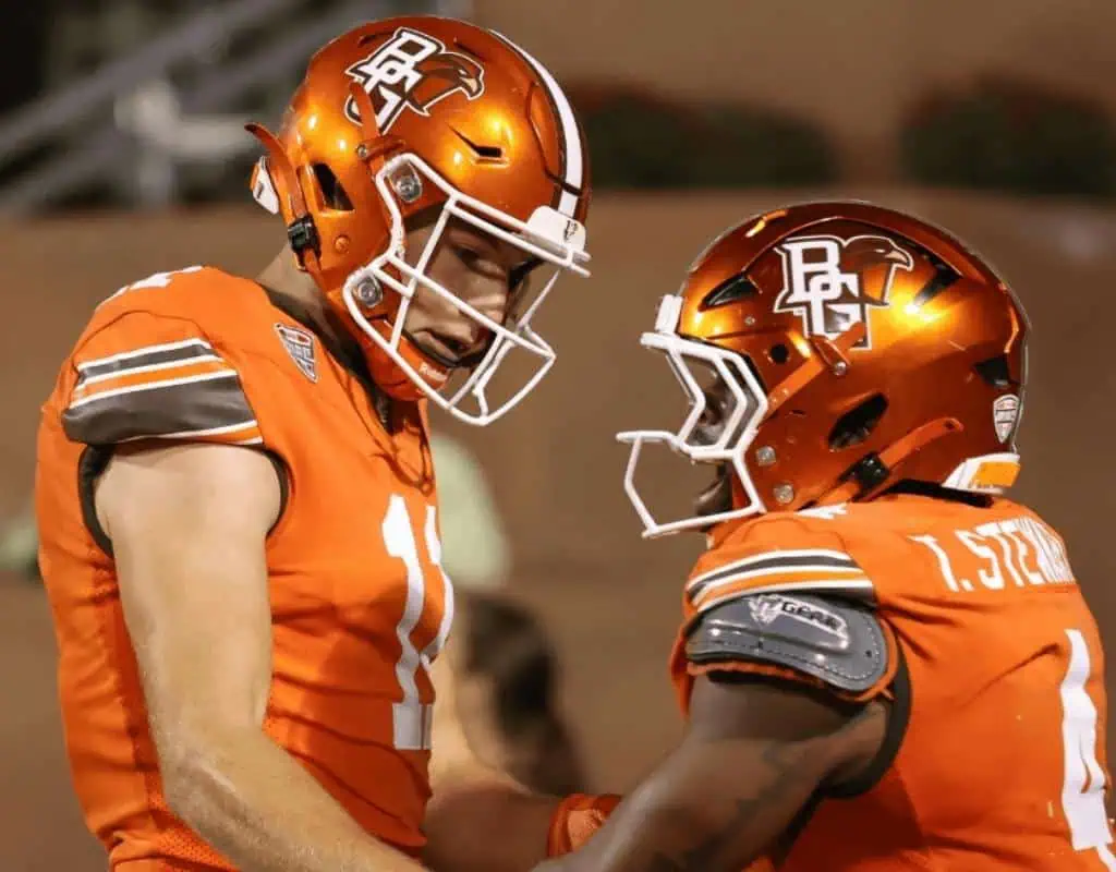 NCAAF 3 Two football players in orange uniforms celebrate on the field under stadium lights, showcasing their team's logo and gear.