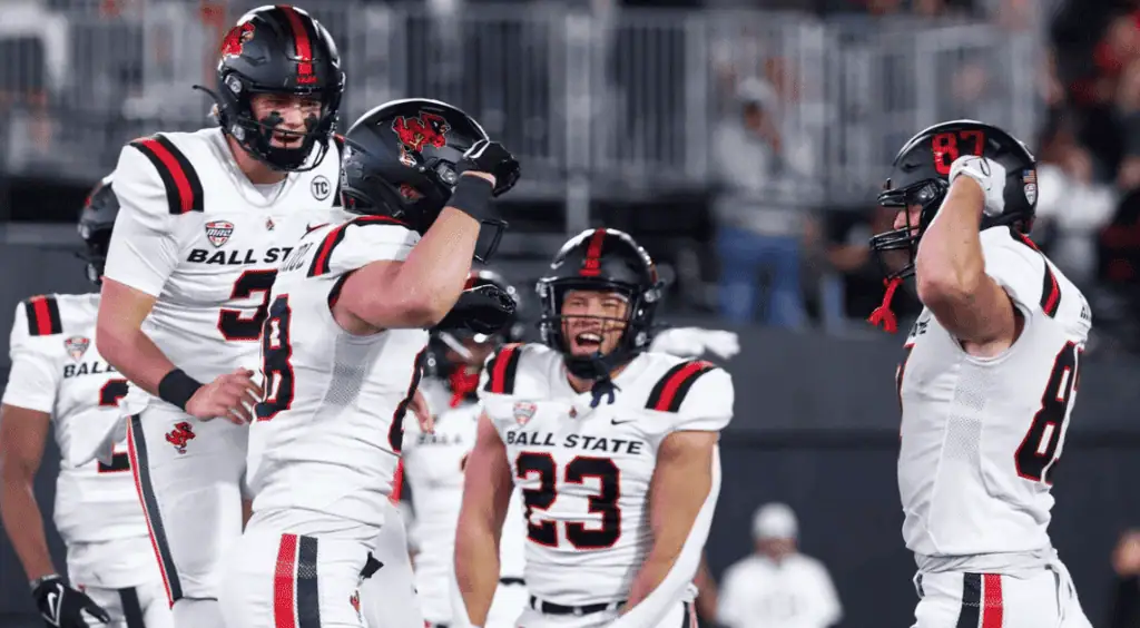 NCAAF 3 Ball State football players celebrate on the field wearing their black and white uniforms, showcasing team spirit and excitement.