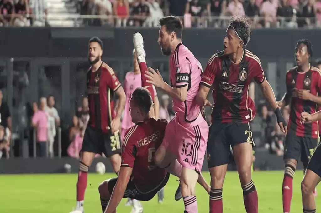 A tense soccer match moment with players in red and black jerseys challenging one another, showcasing dynamic athletic action on the field.