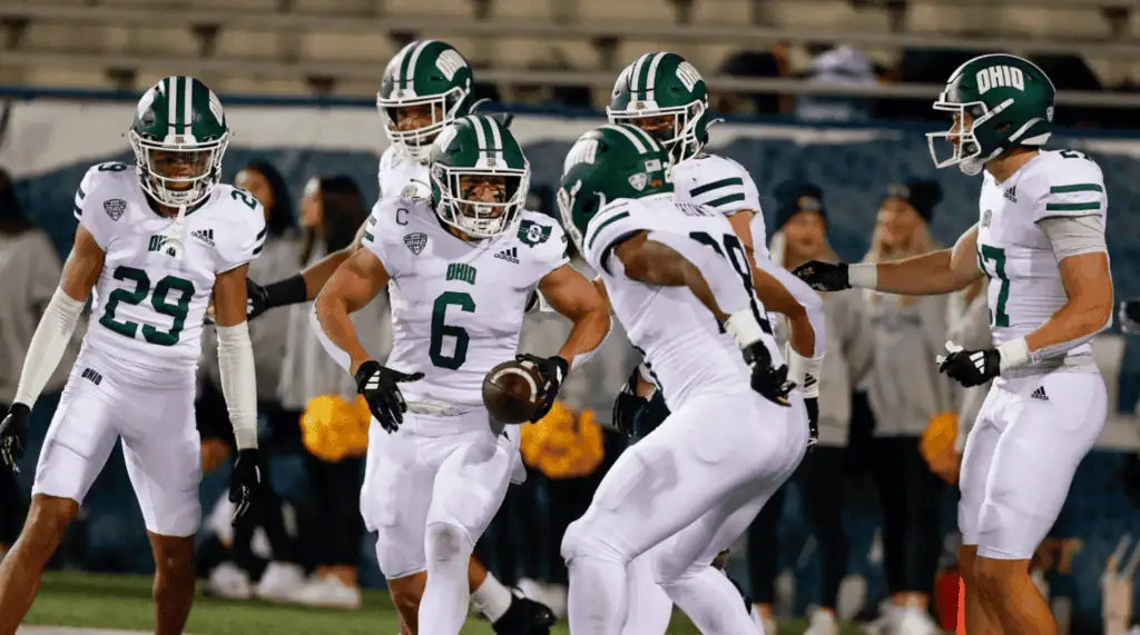 NCAAF 2 A football team in white uniforms celebrates a play on the field, with players showcasing teamwork and excitement during a game.