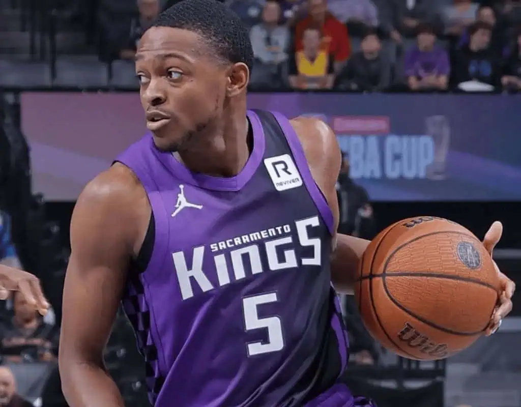 A player in a purple Sacramento Kings jersey dribbles a basketball during a game, showcasing dynamic movement and focus.
