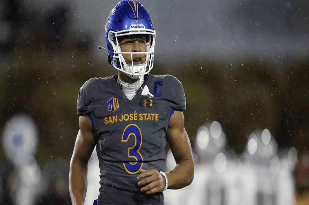 NCAAF 4 A football player in gray San Jose State uniform, wearing a blue helmet, runs on the field during a rain-soaked game night.