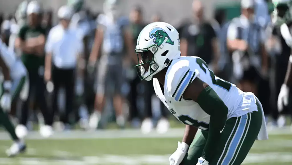 NCAAF 8 A football player in a green and white uniform stands ready on the field, focused and poised for action during a game.