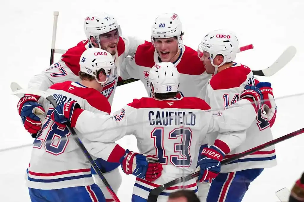 Montreal Canadiens players in white and red uniforms huddle together in celebration on the ice after a goal.