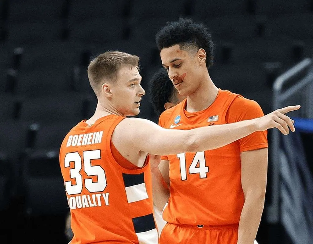 Two basketball players in orange uniforms engage in conversation on the court, strategizing during a game.