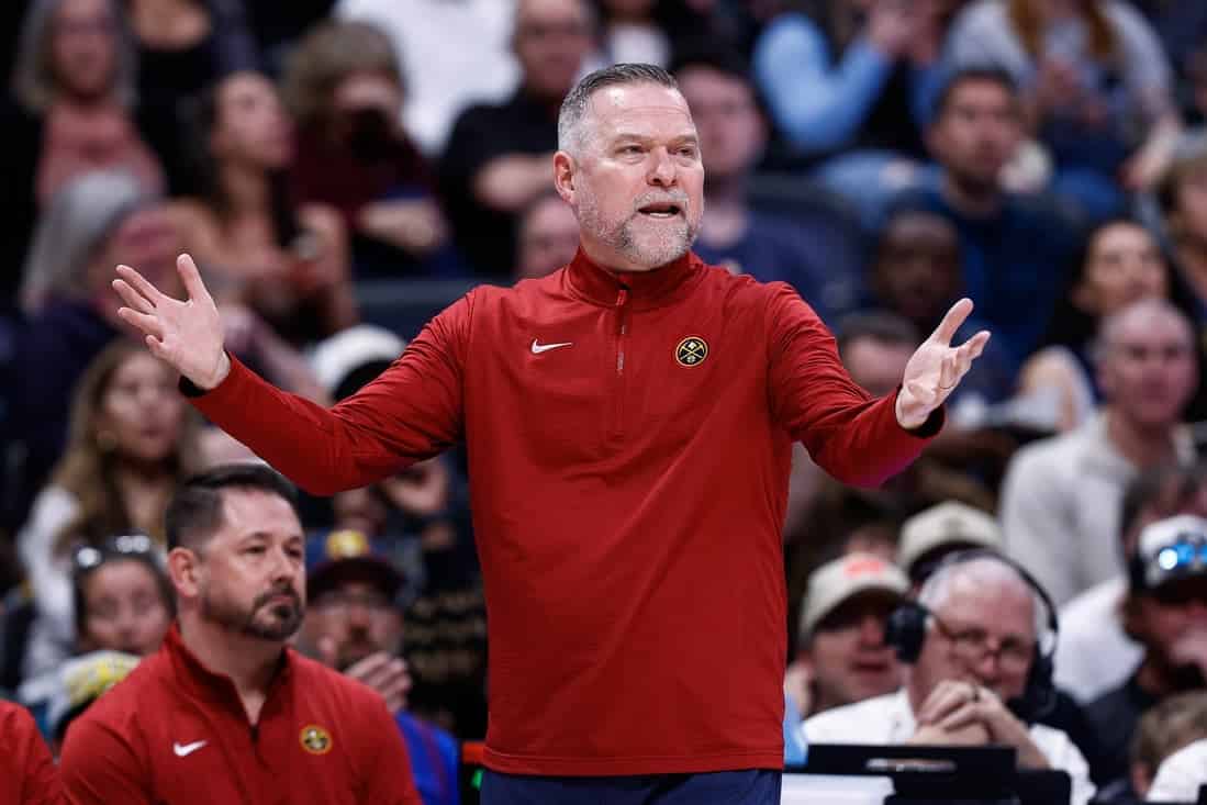 10 A coach in a red jacket gestures passionately during a basketball game, while fans watch intently in the background.