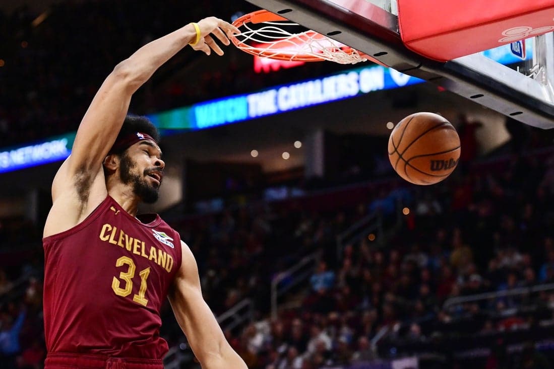 A Cleveland Cavaliers player in a maroon jersey dunks a basketball into the hoop, showcasing athleticism in a packed arena.