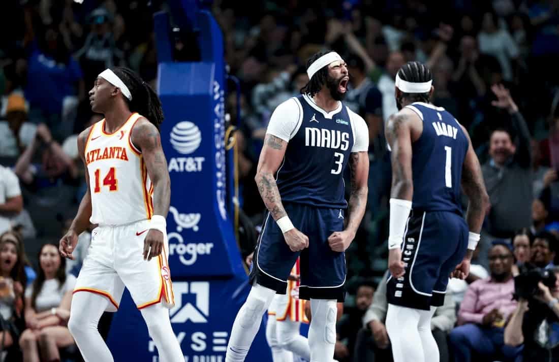 Two basketball players in dark uniforms celebrate on the court while another player in a light uniform looks on during a game.