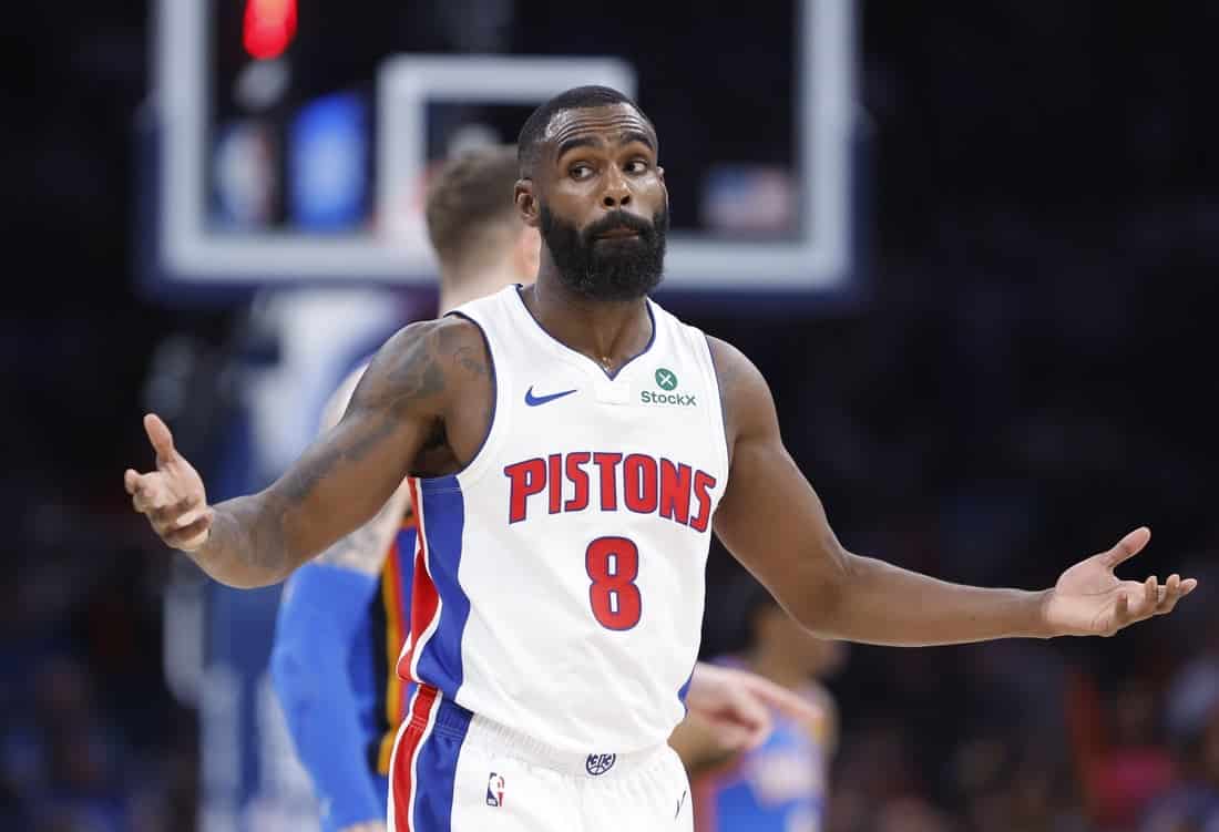 A Pistons player in a white jersey with the number 8 holds out his arms in disbelief during a game, with teammates in the background.