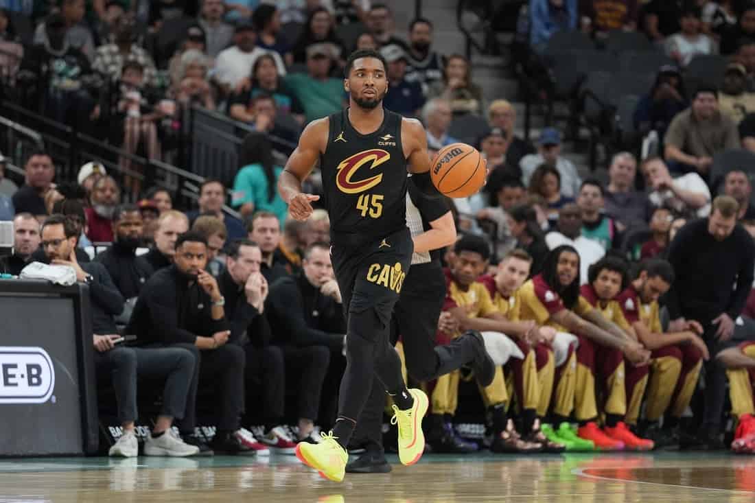 3 A basketball player in a black jersey with "Cavs" logo dribbles the ball during a game, with spectators and teammates in the background.