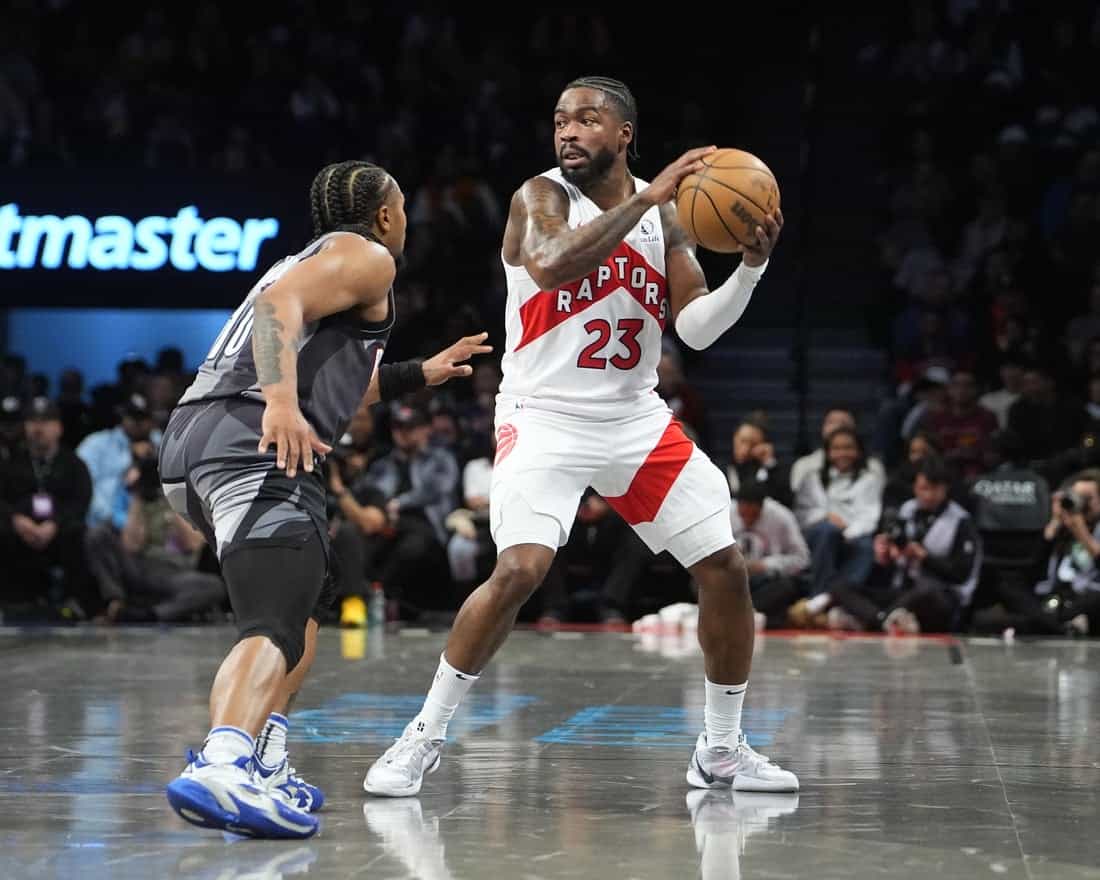 7 A Toronto Raptors player wearing white and red jersey prepares to pass while being closely guarded by an opponent in a basketball game.