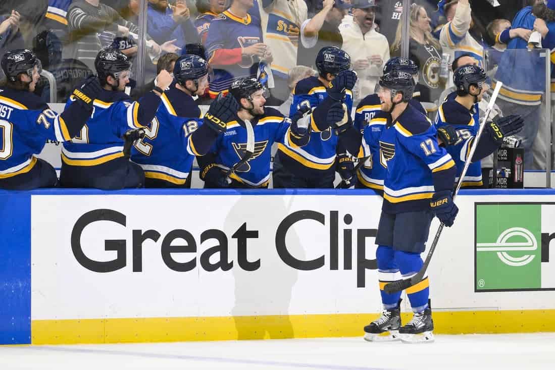 NHL 7 A group of hockey players in blue jerseys celebrate on the bench, with cheering fans visible in the background.