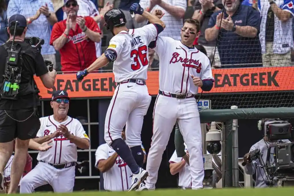 A baseball player in a white jersey celebrates a home run with teammates, while fans cheer enthusiastically in the background.