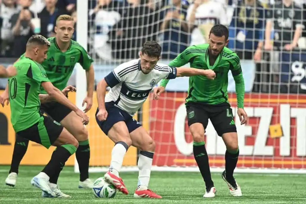 A tense soccer match scene featuring players in green and white jerseys, battling for possession near the goal line.