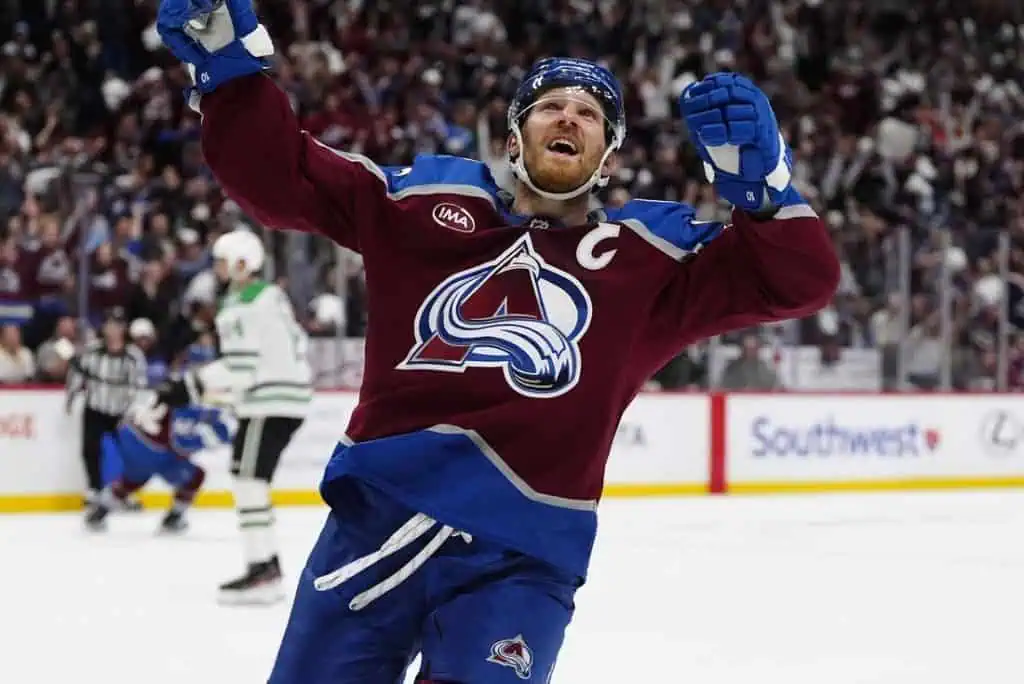 NHL 5 A hockey player in a maroon jersey celebrates a goal, raising his arms in triumph amidst a cheering crowd.