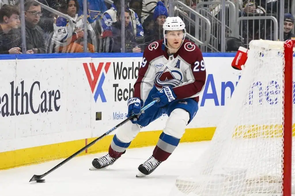 A player from the Colorado Avalanche, wearing a white jersey with red accents, stands on the ice, ready for the game.