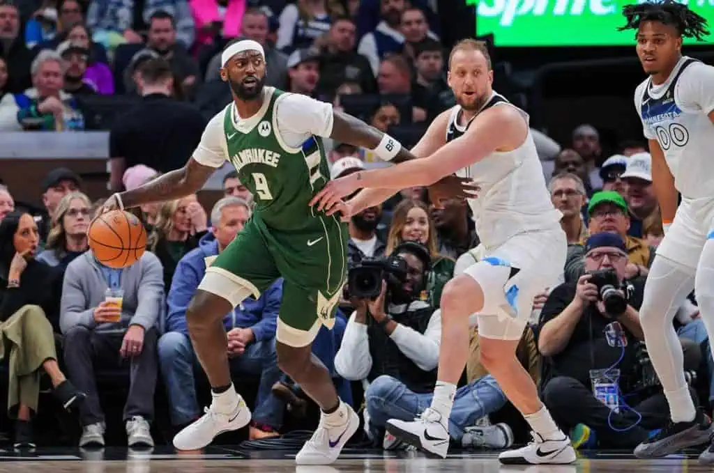 3 A basketball player in a green Milwaukee jersey dribbles while being closely guarded by an opponent in a white jersey during a game.