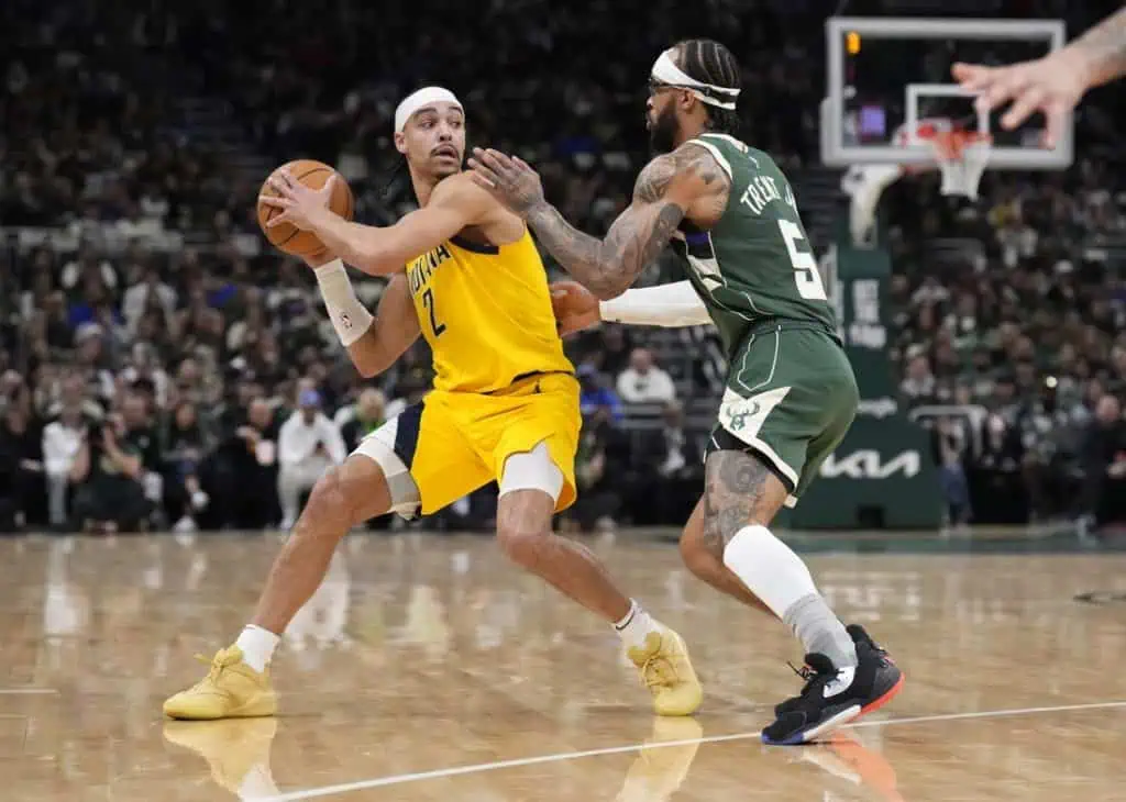 A basketball player in a yellow jersey dribbles a ball while closely guarded by an opponent in a green jersey during a game.