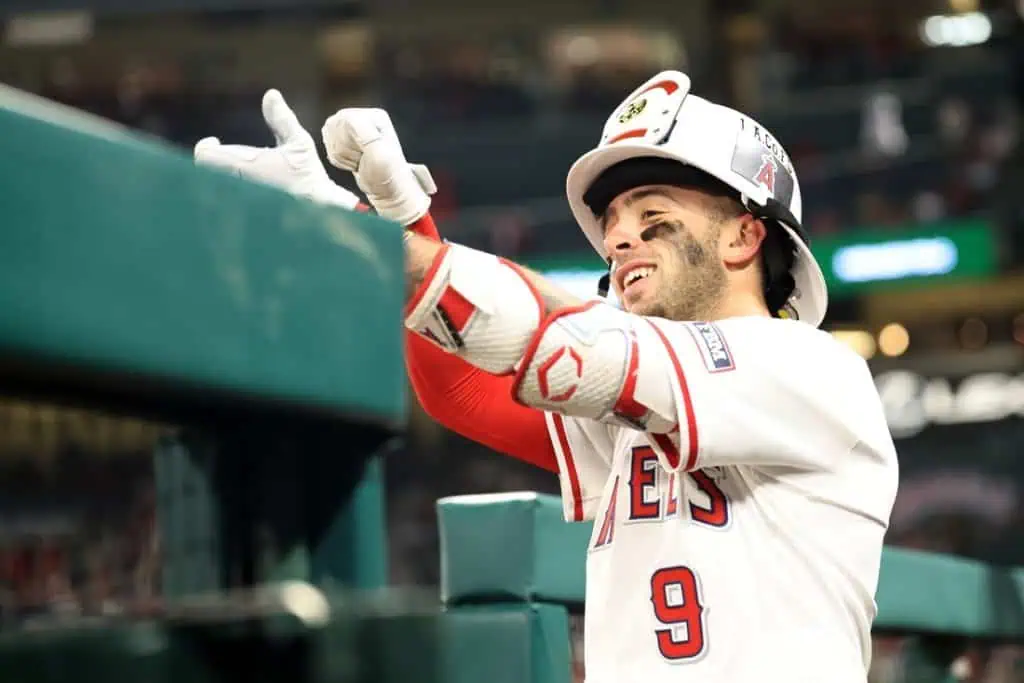 A baseball player in a white jersey with red accents gestures enthusiastically from the dugout, showcasing team spirit and excitement.