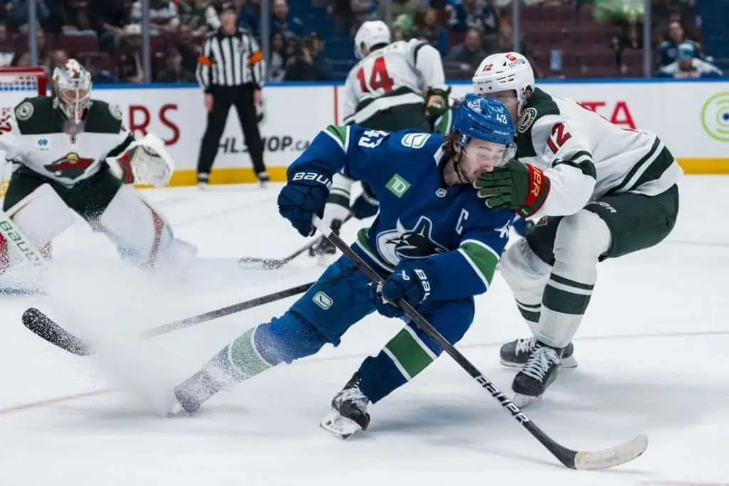 NHL 10 A player in a blue hockey jersey struggles for control of the puck amidst a flurry of ice, with opponents in green nearby.