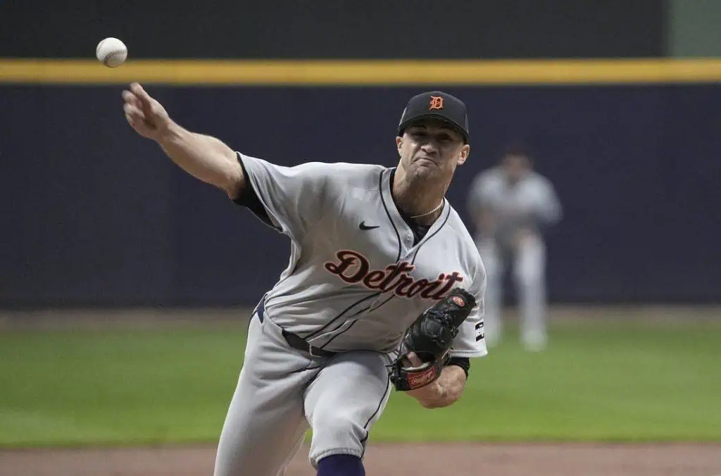 A Detroit Tigers pitcher in a gray uniform winds up to throw a baseball during a night game on a baseball field.