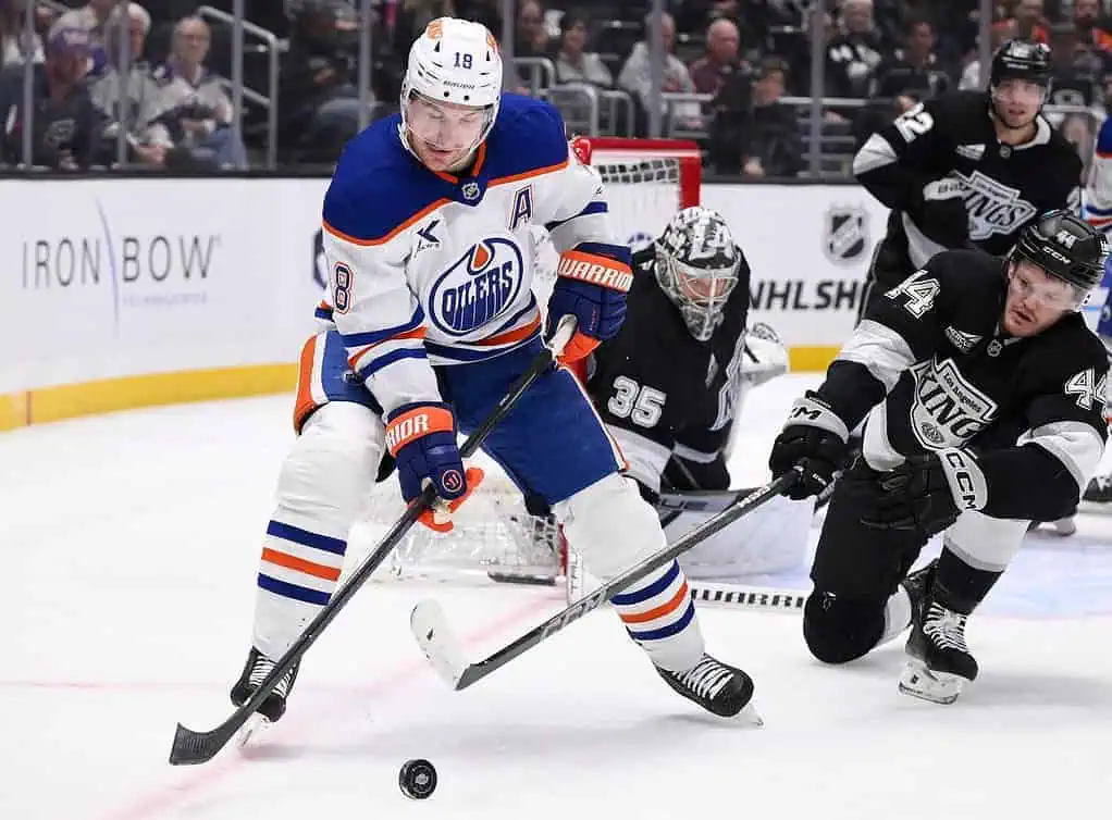 An Edmonton Oilers player maneuvering the puck while being defended by a Los Angeles Kings player during an intense hockey match.