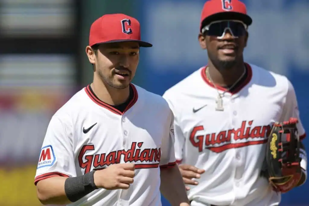 Two baseball players in white and red "Guardians" jerseys, smiling and jogging together on a sunny field.
