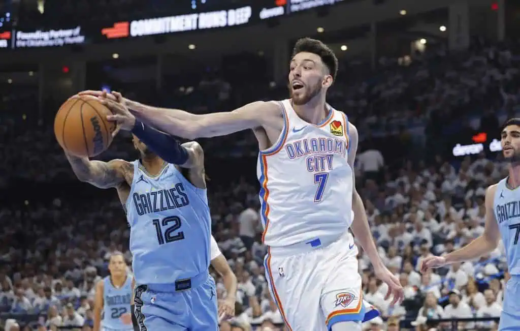 A player in an Oklahoma City Thunder jersey passes the basketball, while a defender in a Grizzlies jersey reaches for it during a game.