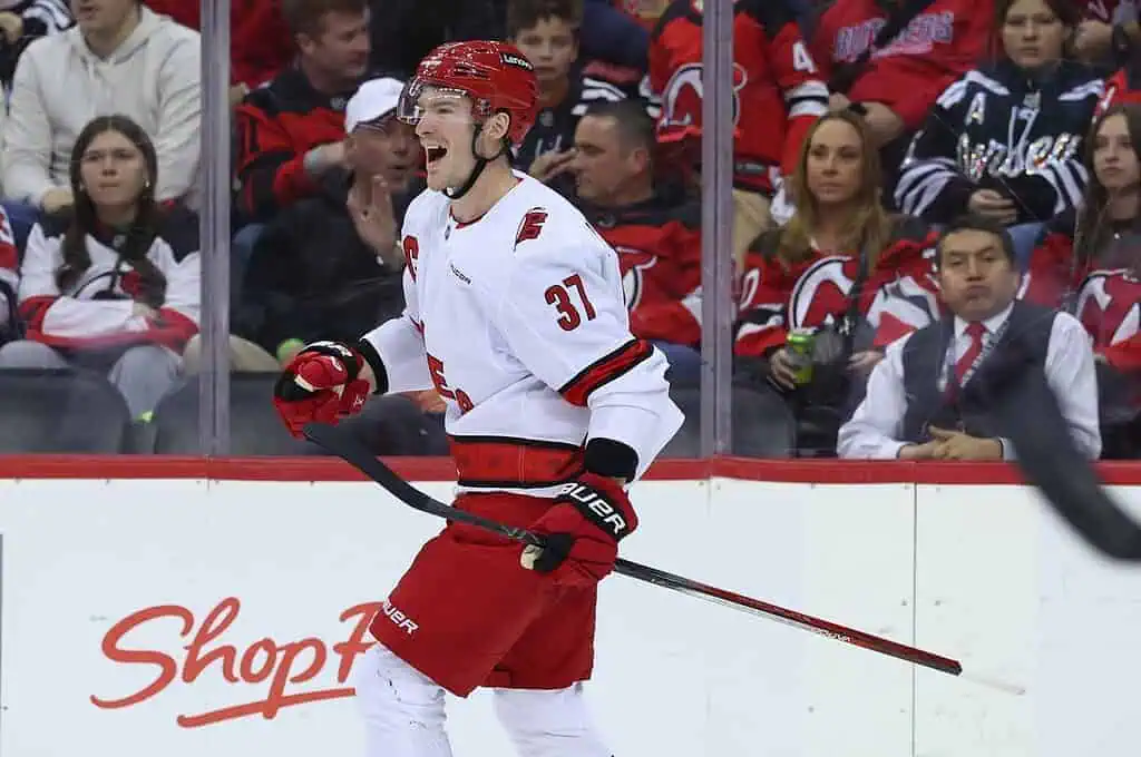 NHL 3 A hockey player in a red and white jersey celebrates on the rink, surrounded by fans in team jerseys at a lively game.