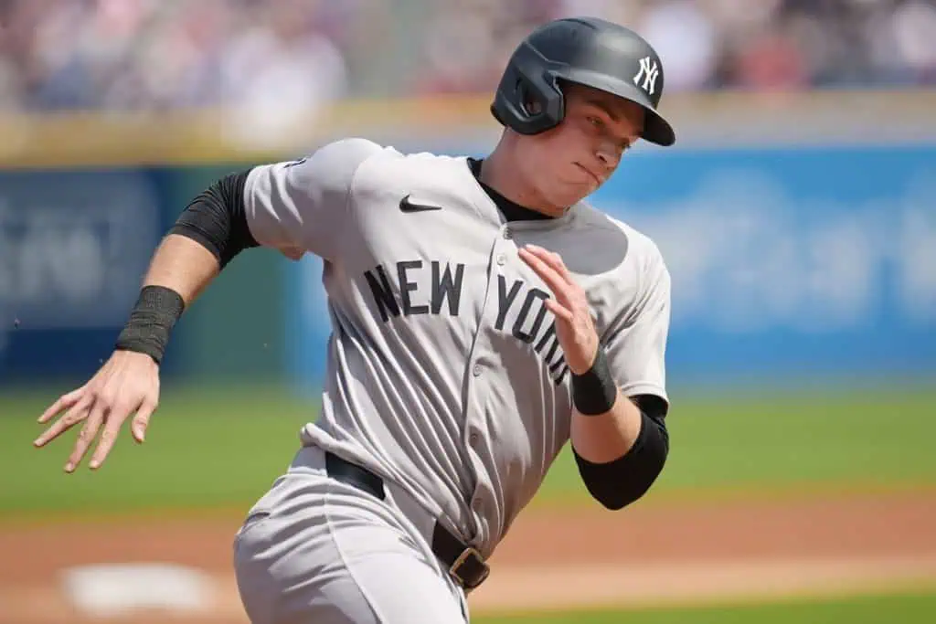 A player in a gray New York Yankees uniform sprints towards first base on a sunny day at the baseball field.
