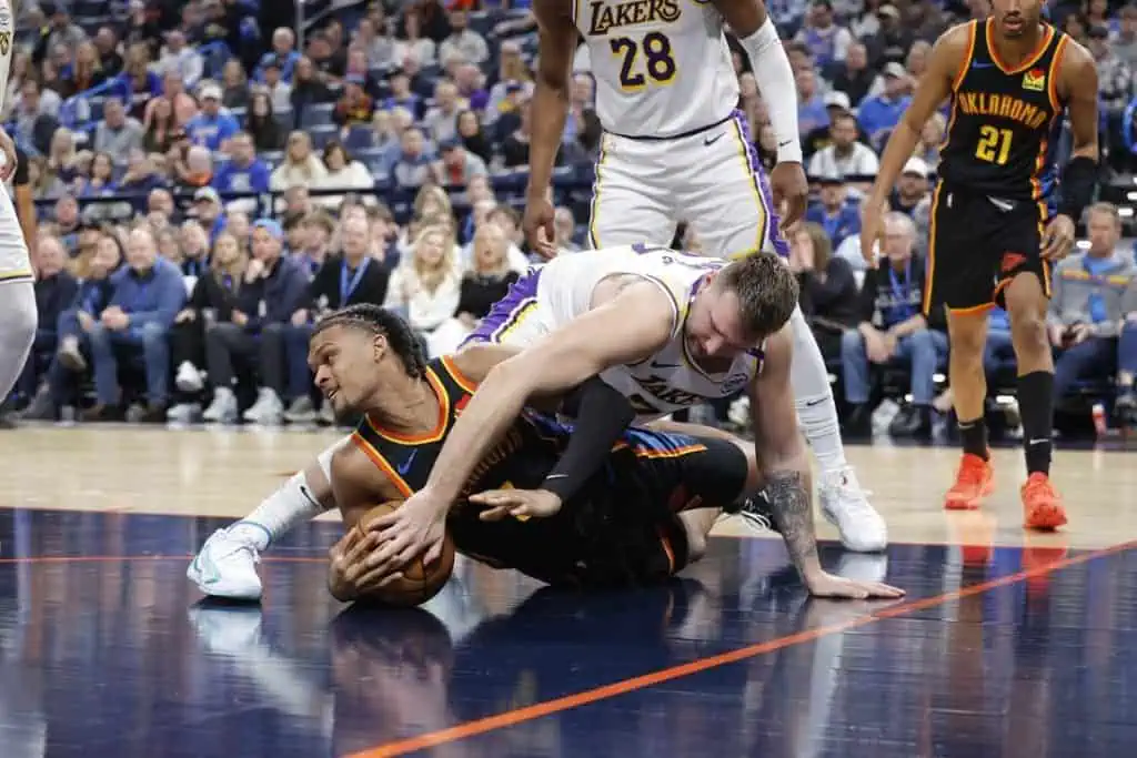 4 Two basketball players struggle for the ball on the court, surrounded by teammates and an engaged crowd in the background.