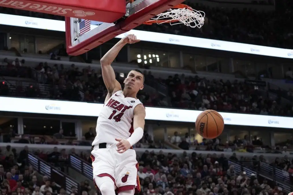 8 A basketball player in a white "Miami Heat" jersey performs a powerful dunk during a game, with fans visible in the background.