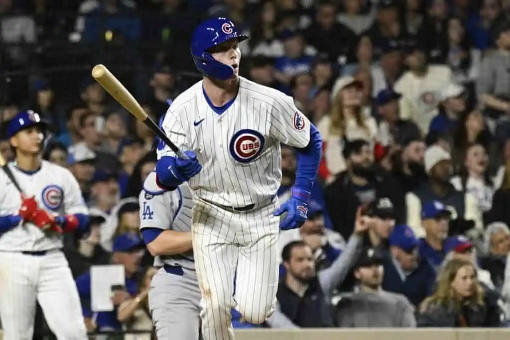A Chicago Cubs player runs excitedly, bat in hand, as fans cheer in the background during a night baseball game.