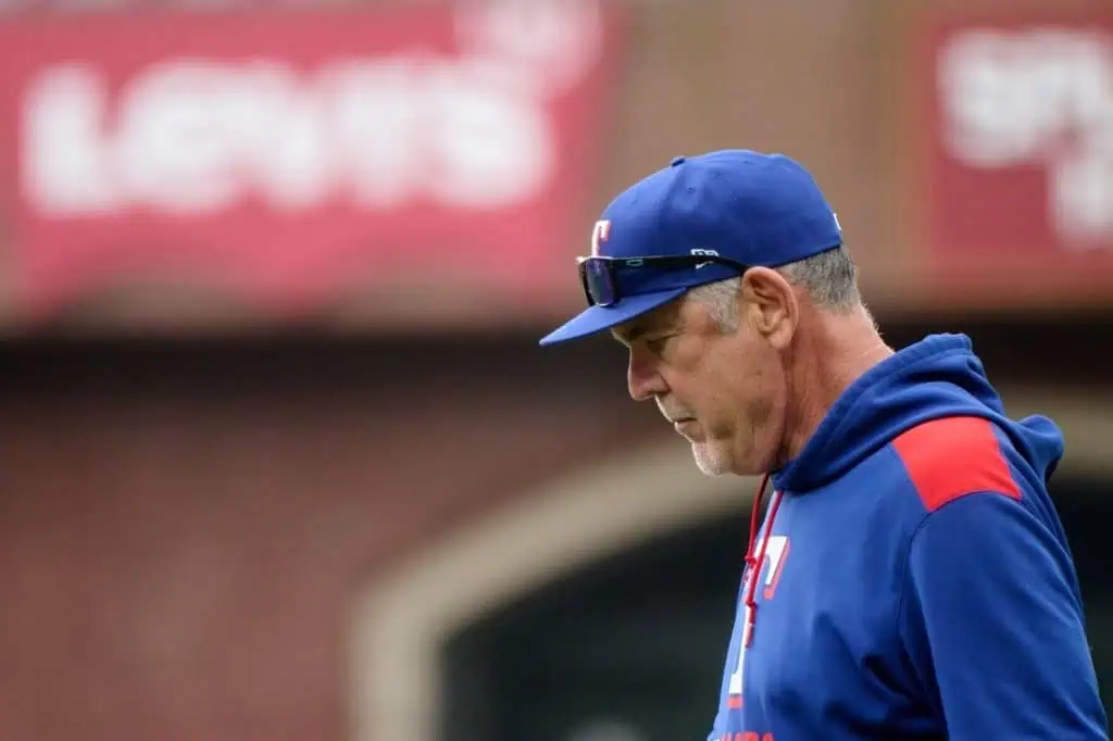 A coach wearing a blue cap and navy sweatshirt walks thoughtfully on the baseball field, with Levi's.