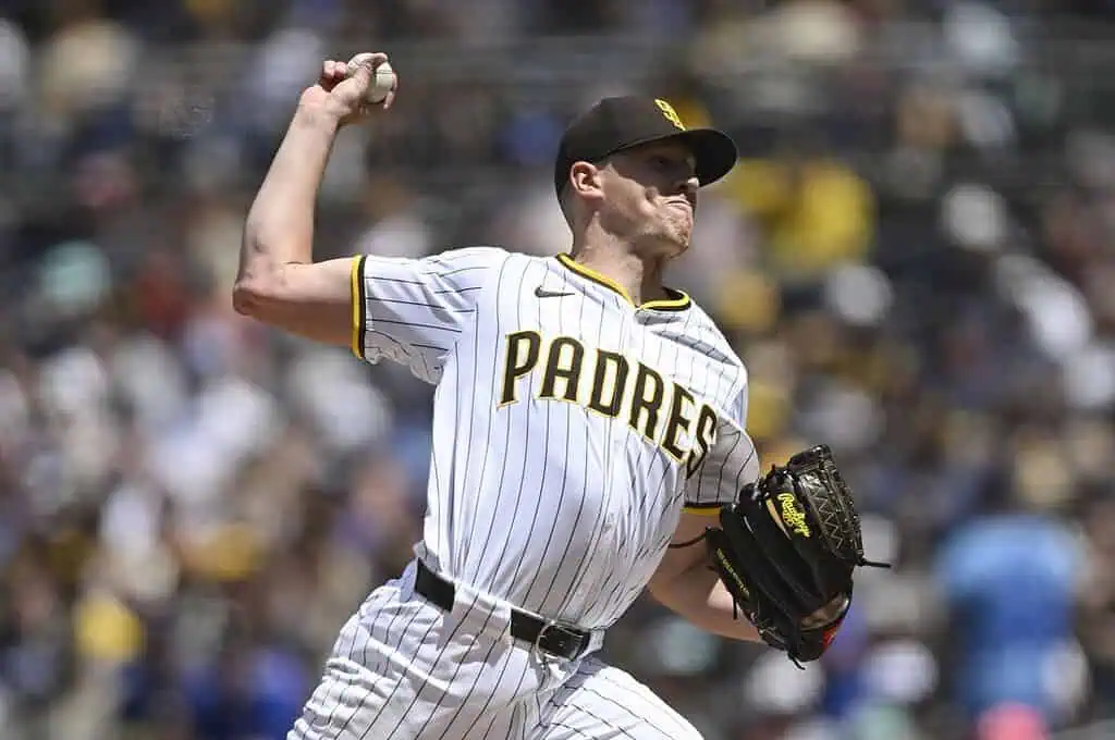 A baseball player in a white and yellow Padres uniform winds up to pitch on a sunny day,