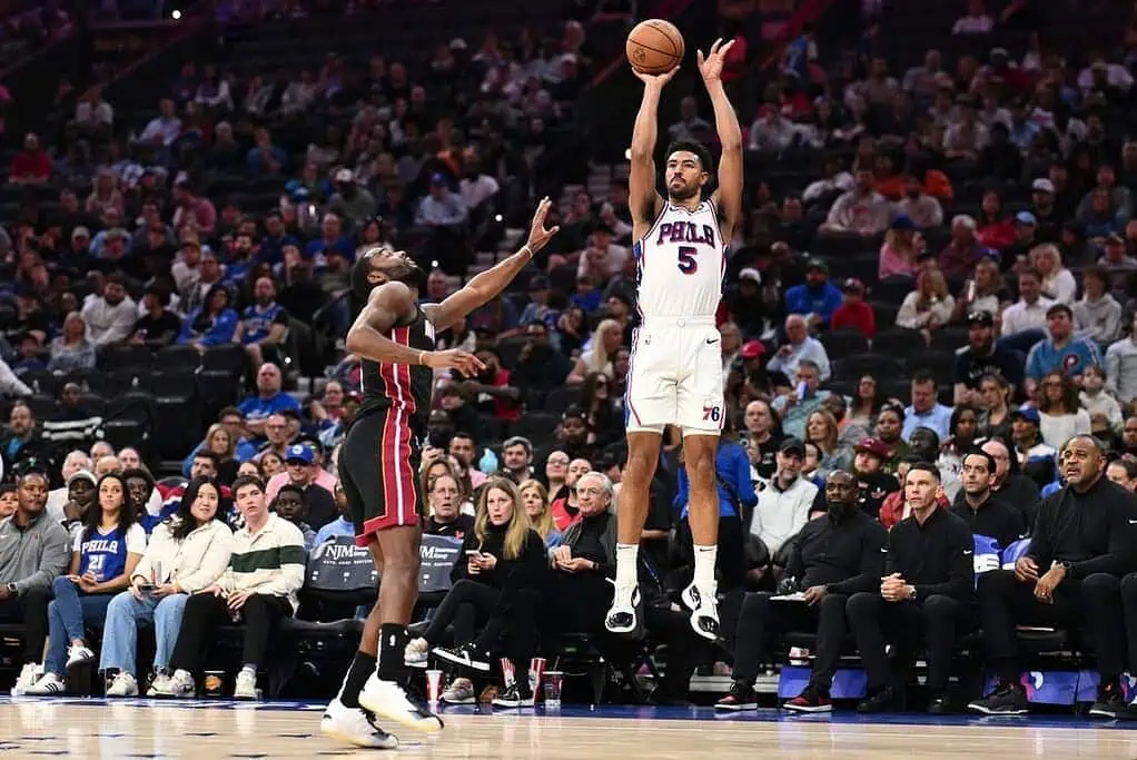 8 A player in a white Philadelphia 76ers uniform jumps to take a shot during a basketball game, with spectators in the background.