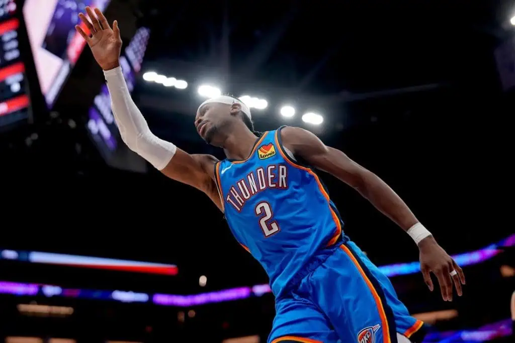 A basketball player in a blue Oklahoma City Thunder jersey waves to the crowd during a game, showcasing enthusiasm and team spirit.