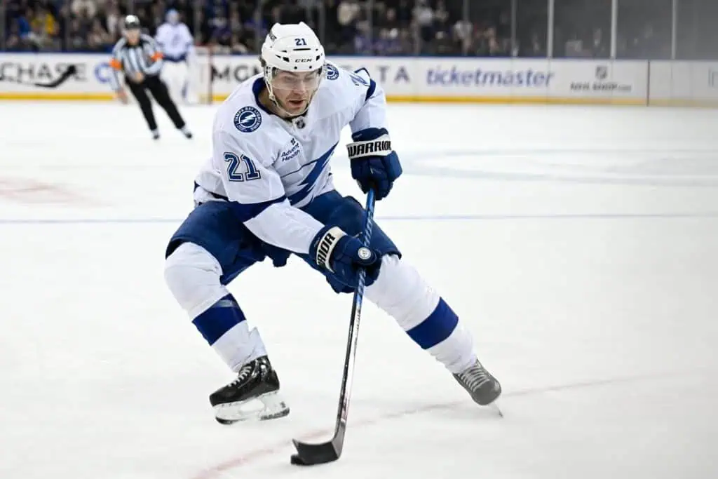 A Tampa Bay Lightning player glides over the ice, preparing to shoot the puck while wearing a white and blue uniform.