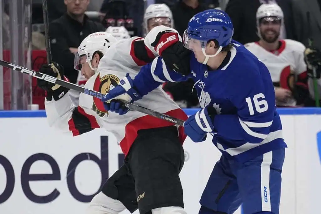 A heated moment in a hockey game as a player in a blue jersey checks an opponent in a red and black jersey against the boards.