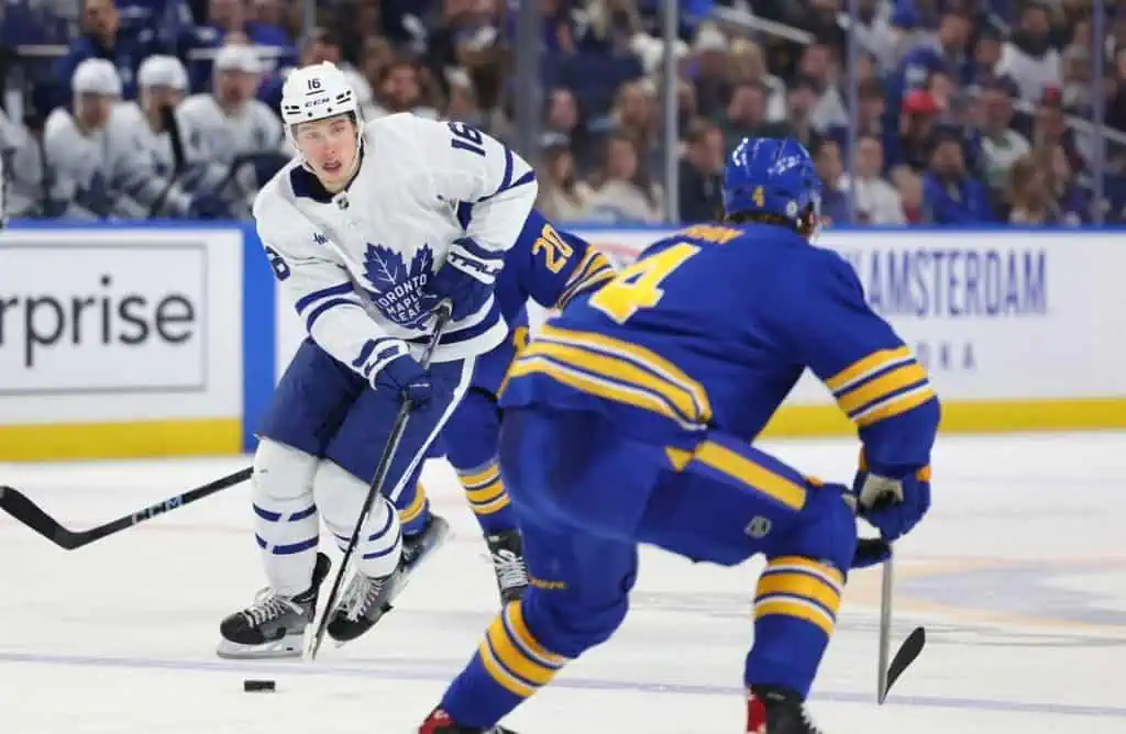 A hockey player in a white uniform maneuvers the puck past an opponent in a blue uniform during an intense game.