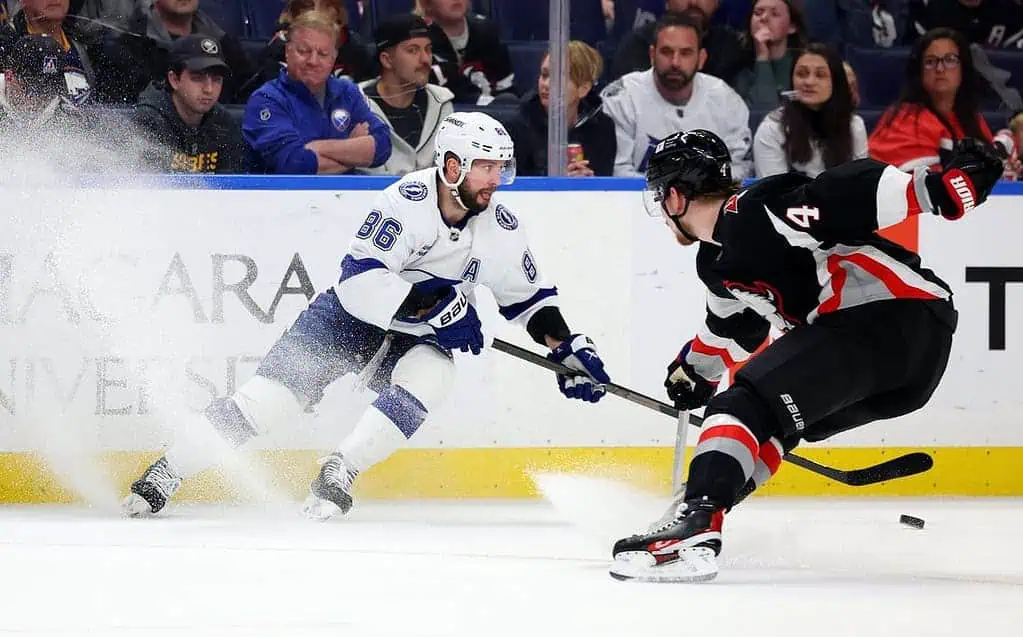 Two ice hockey players compete fiercely for the puck, with snow flying from their skates in an intense game atmosphere.