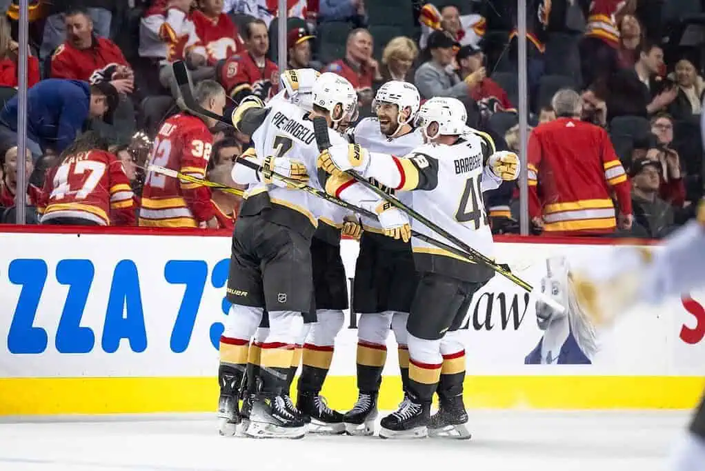 A group of hockey players in black and gold jerseys celebrates a goal, high-fiving each other in a stadium filled with fans.