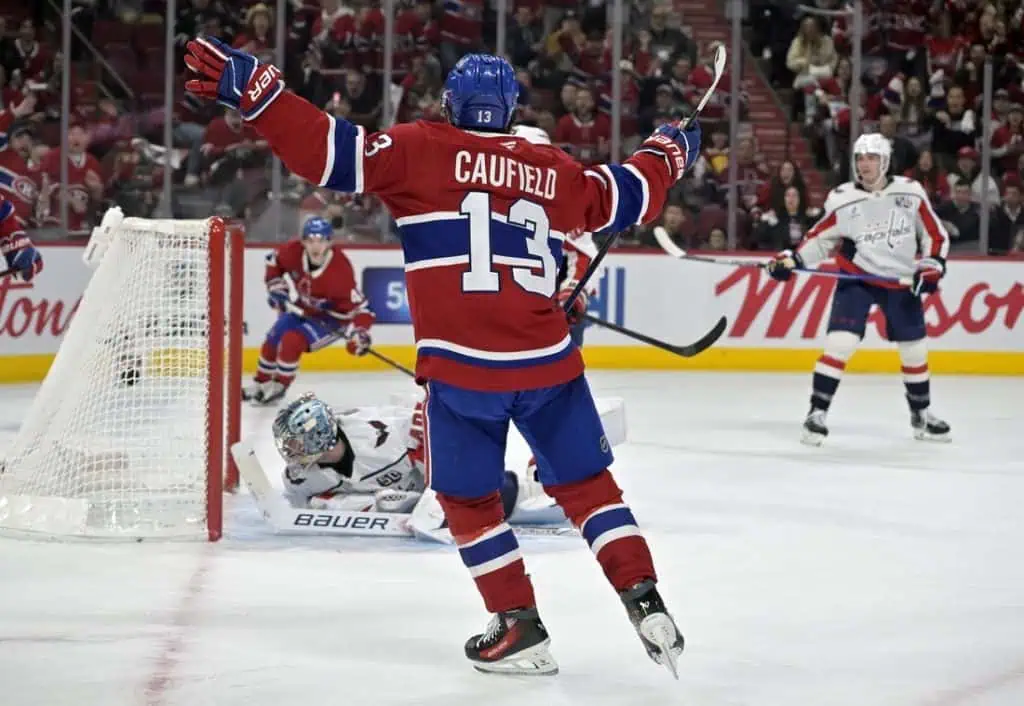 NHL 9 A Montreal Canadiens player, Caufield, celebrates a goal as the puck is in front of the goalie, amidst a packed arena.